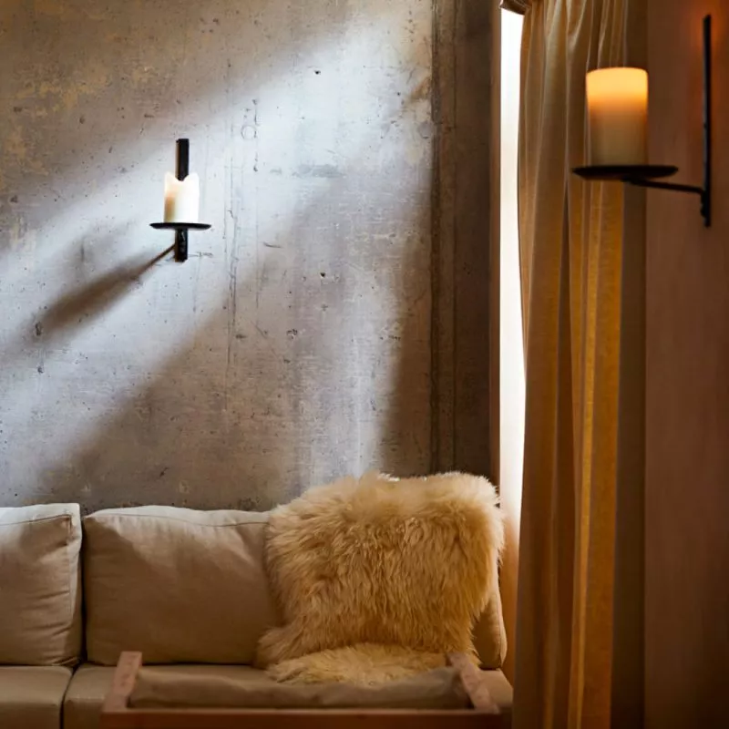 Interior image of restaurant St. Barts in an intimate corner, bare concrete walls with candle holders, linen curtains, a sofa with a sheep wool throw