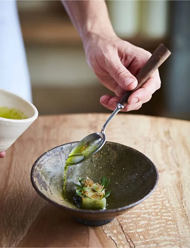 A refined dish being prepared in a small bowl at restaurant St. Barts. A chef pours a gree oil to finish the dish.